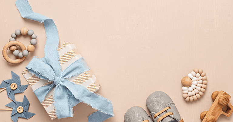 Baby gift box with baby shoes, wooden toys and soft blue ribbon arranged on a neutral background.